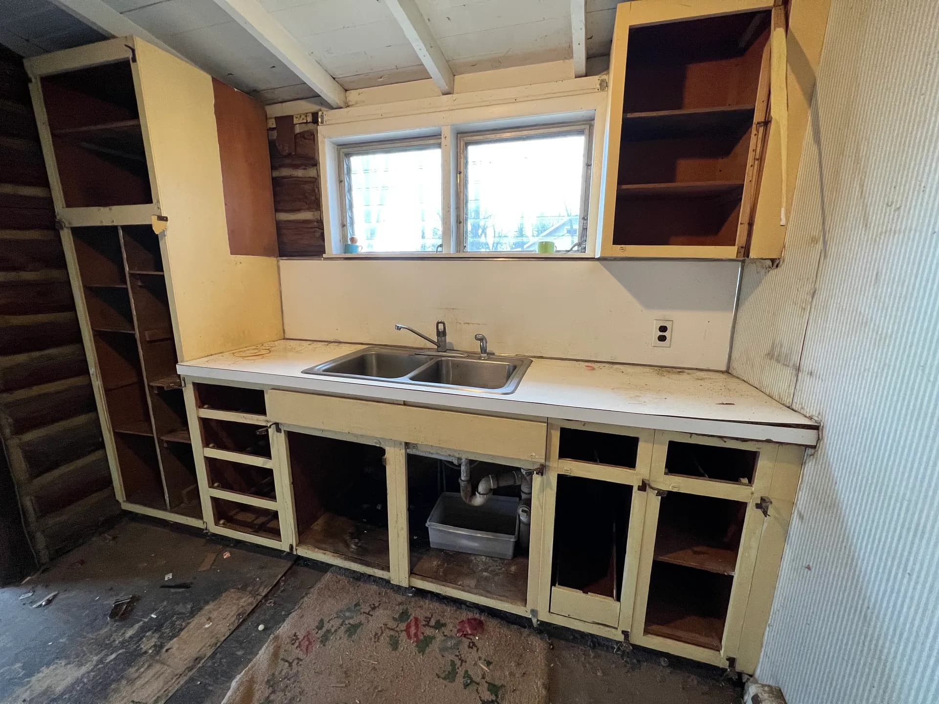 Original kitchen before renovation — doorless cabinets and exposed plumbing