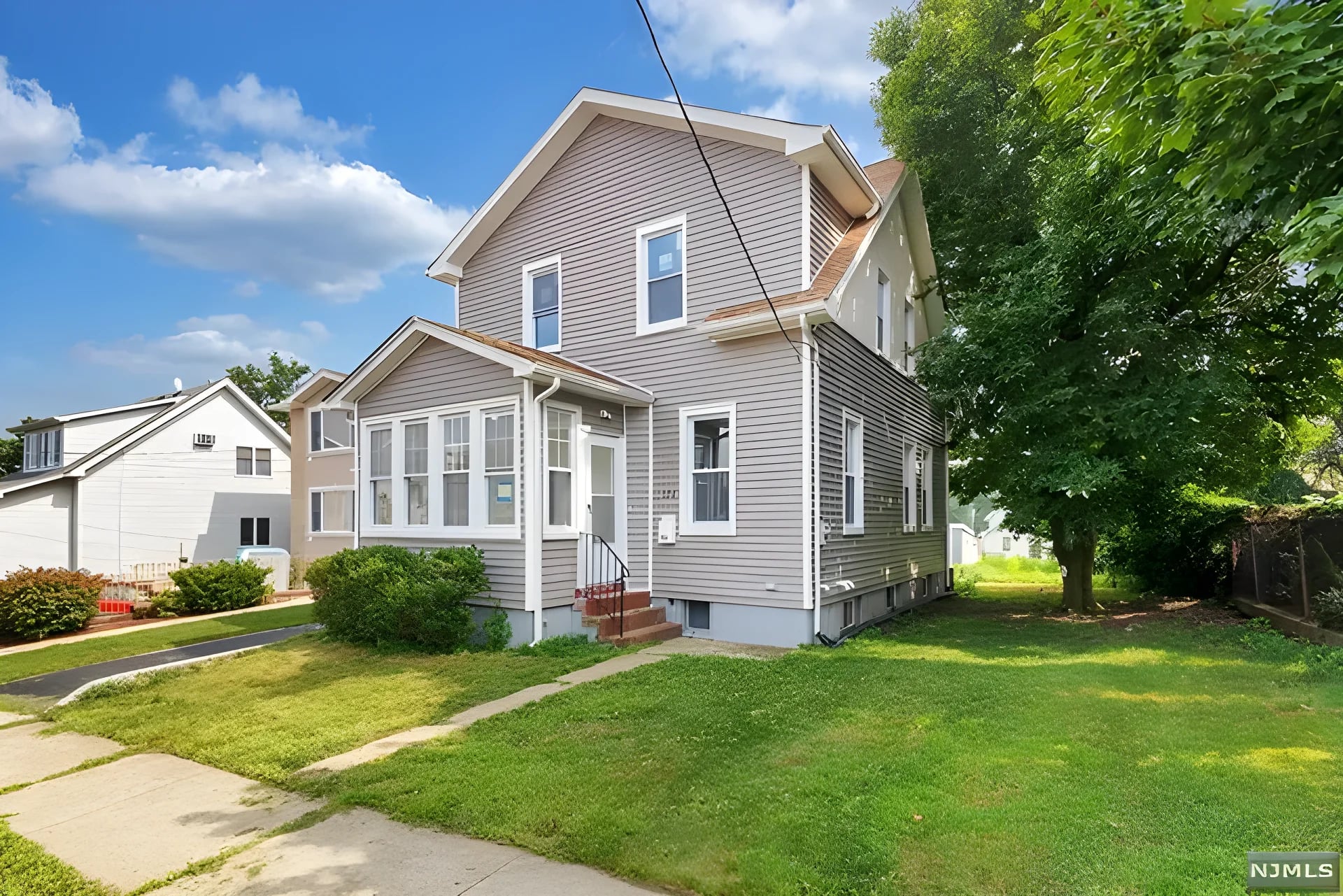 Full front elevation after renovation — new grey siding, enclosed sun porch, and landscaping