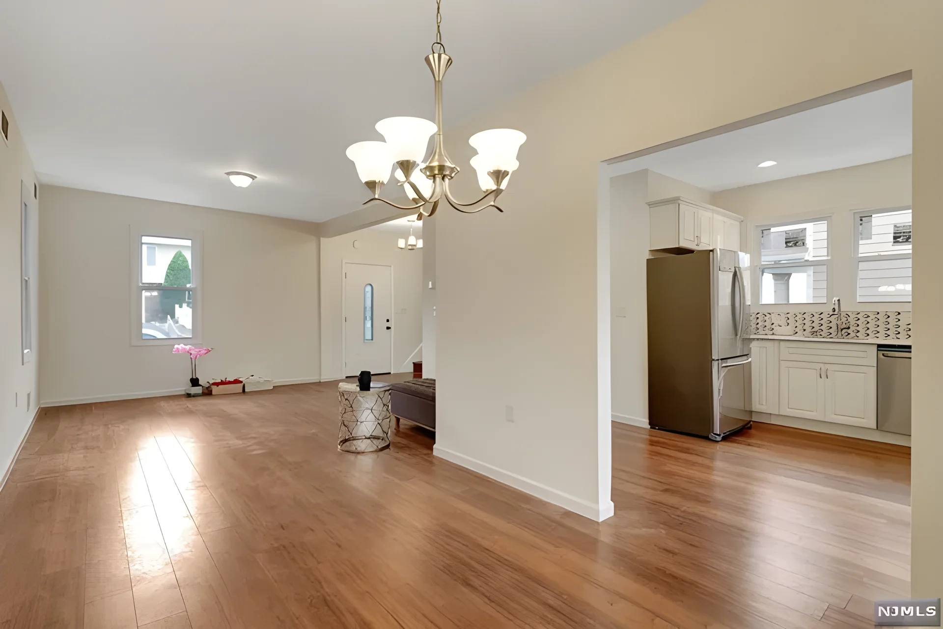 Open living and dining area after renovation — hardwood floors, chandelier, and renovated kitchen beyond